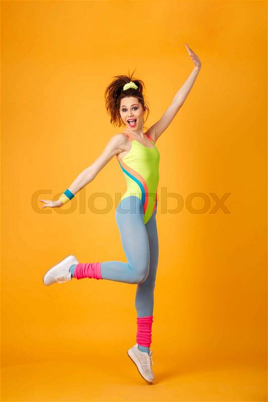 Happy excited young fitness woman jumping and having fun over yellow background, stock photo