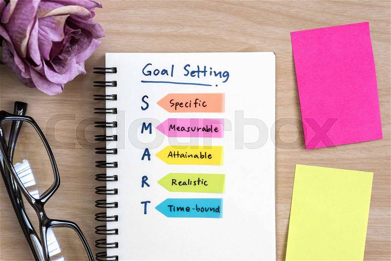 Hand writing definition for smart goal setting on notebook with eye glasses, purple rose and colorful sticky note on desk, stock photo