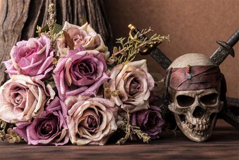 Bouquet purple roses with pirate skull and two swords over tree background on wooden table still life style halloween concept, stock photo