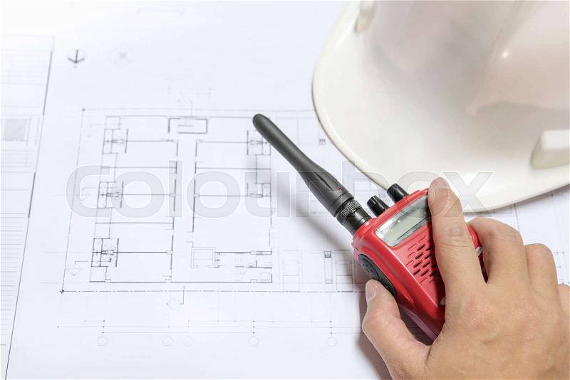 Engineer hand holding radio communication on architectural blueprints paper near helmet, architect engineering and contractor concept, stock photo
