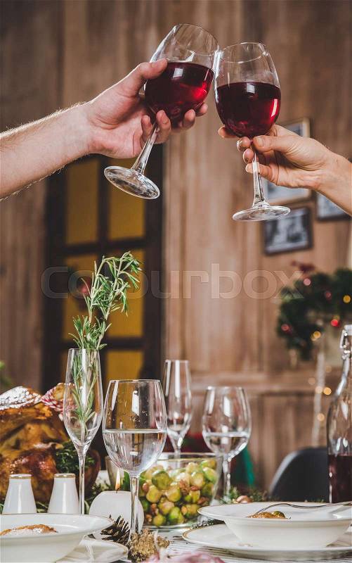 Partial view of couple toasting glasses of red wine at Christmas dinner, stock photo