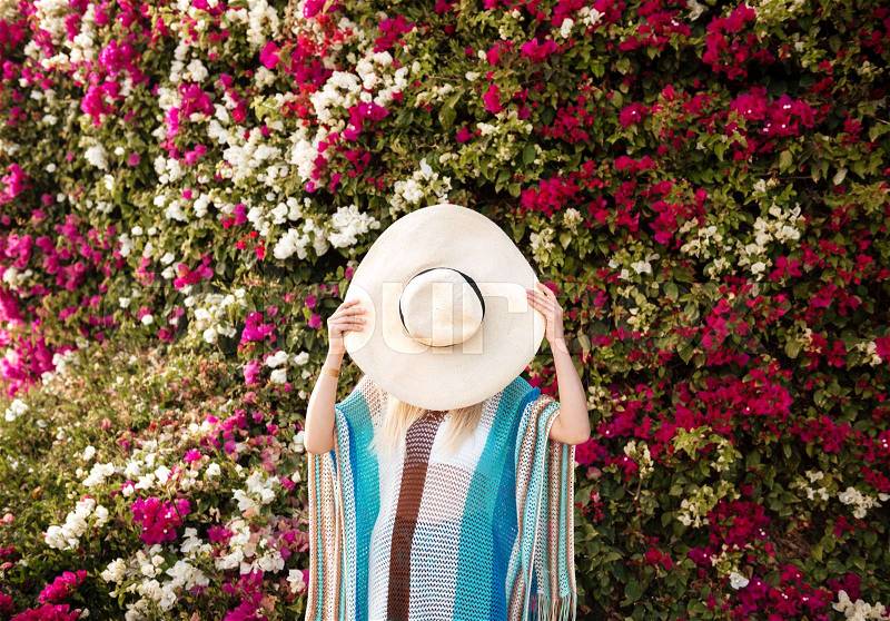 Woman in beachwear which hiding behind the hat with flower bush on background, stock photo