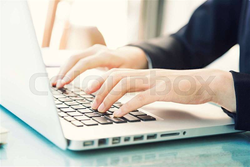 Female hands of business woman typing on computer laptop keyboard, soft window light, selective focus on fingers, vintage retro color style, stock photo