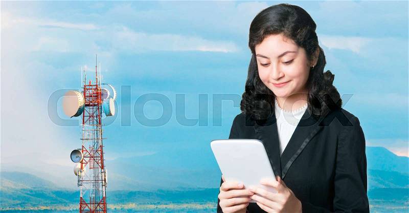Attractive bussiness woman using computer tablet with telecommunication tower against mountain range during sunset in background, stock photo