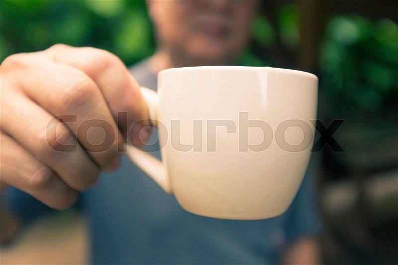 Man holding out a white coffee cup, in vintage tone, selective focus with blurred foreground and background, stock photo