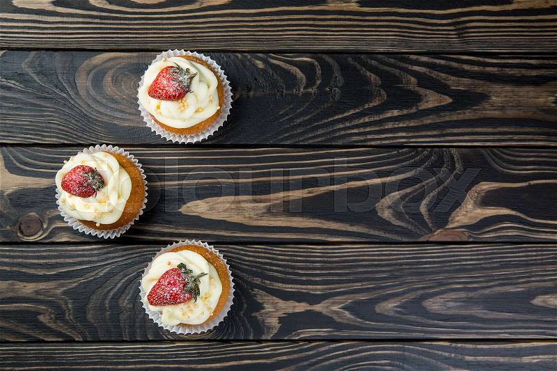 Strawberry cupcakes on wooden background. Tasty cupcake with strawberry on dark wooden background, stock photo