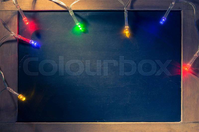 Strip of colorful Christmas lights on top of small blackboard with beam of hard light and vintage retro color tone, stock photo