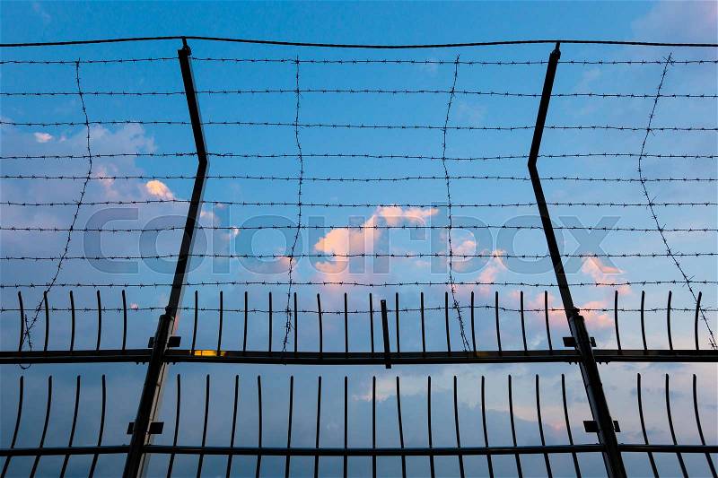 Barbed wire fence silhouettes against cloudy dark blue sky at sunset, stock photo