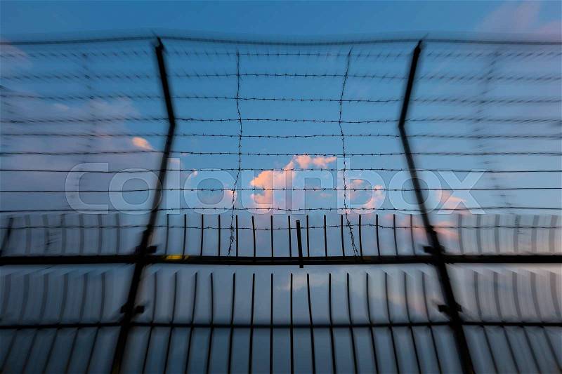 Barbed wire fence silhouettes against cloudy dark blue sky at sunset with blur effect, stock photo