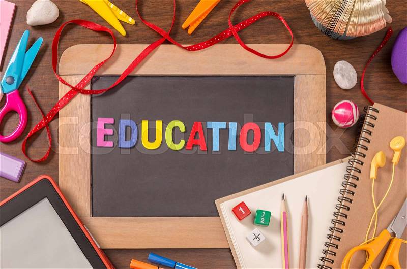 Education word formed by color wooden alphabets on small blackboard with school supplies on wooden table, stock photo