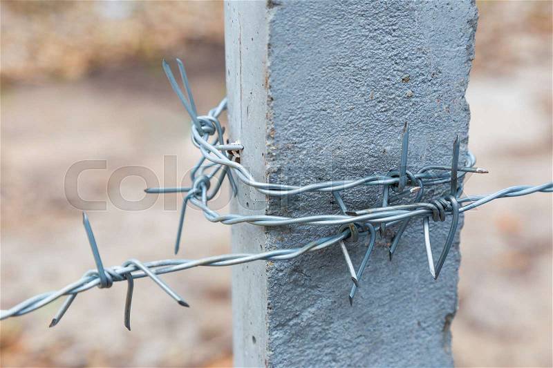 Barbwire wrapped around concrete post, selective focus with blurred background, stock photo