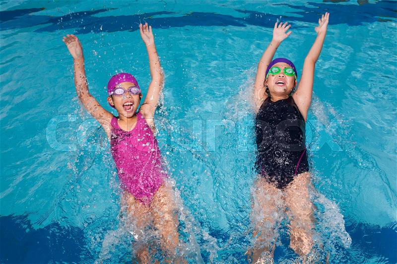 Two sisters jumping backward into swimming pool, having a good time, stock photo