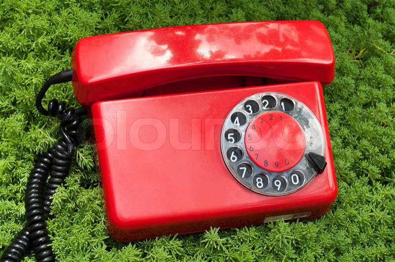 Red and old telephone on a green grass background, stock photo