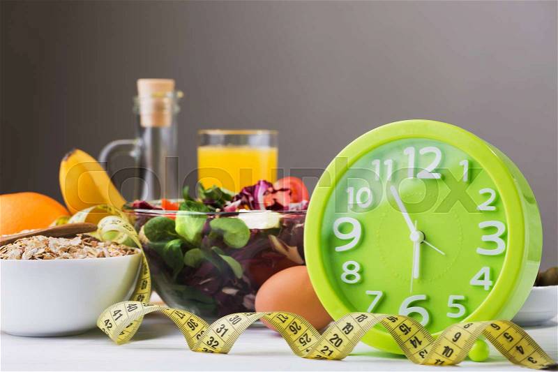Diet concept with green time clock and health food with measuring tape, stock photo