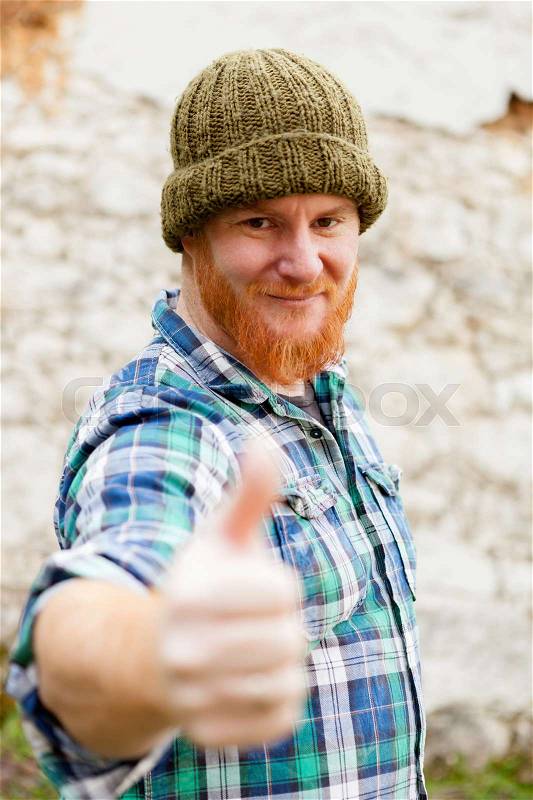 Red haired man with blue plaid shirt and wool hat saying Ok, stock photo