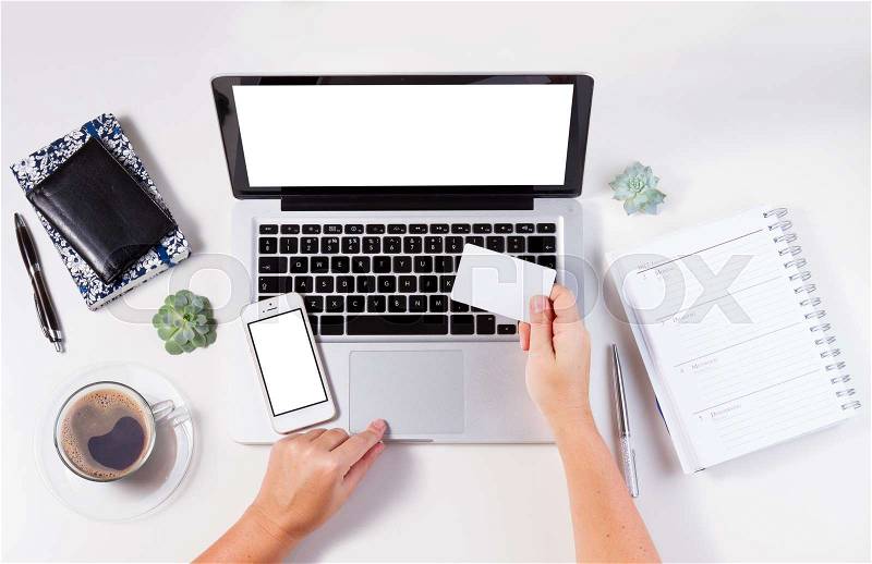 On-line shopping concept mock up - desktop with laptop and hands holging credit card, copy space on empty screen of phone, notebook and plastic card, stock photo