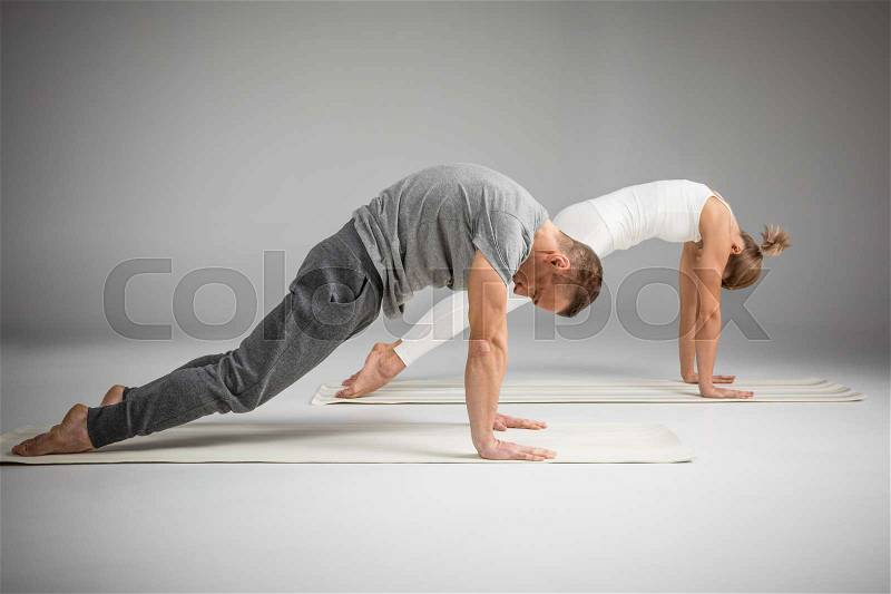 Couple practicing yoga performing cat position on yoga mats, stock photo