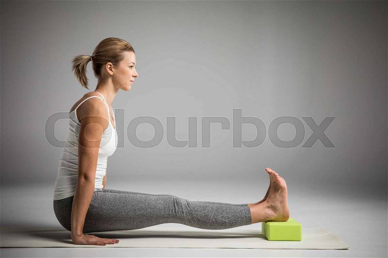 Woman practicing yoga in Angusthasana handstand pose with yoga block, stock photo