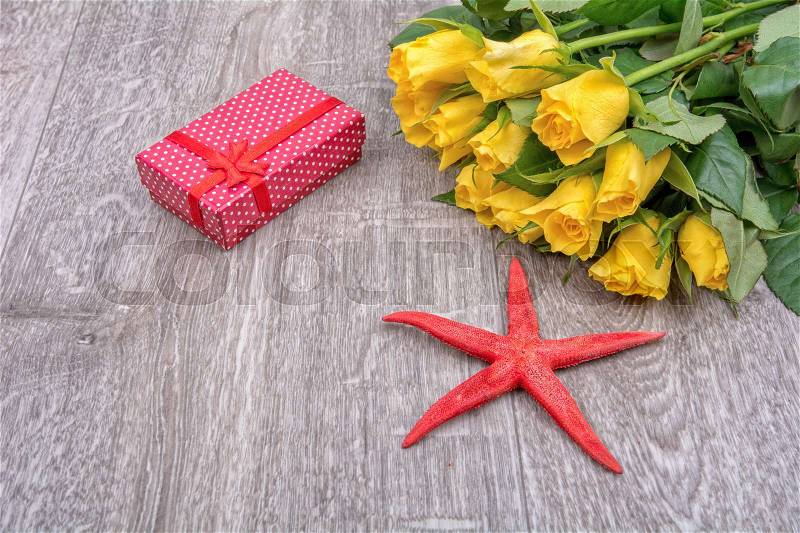 Yellow roses, red gift and red starfish on grey wooden background, stock photo