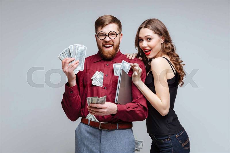 Cunning Woman stick to Male nerd with money. Isolated gray background, stock photo