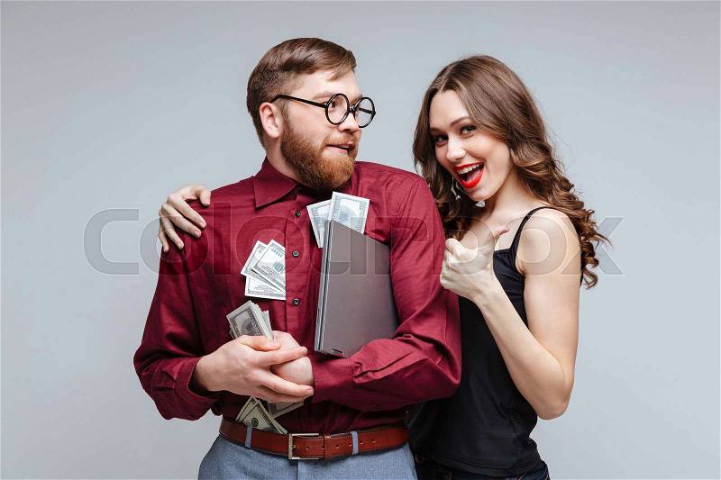 Happy Woman stick to Male nerd with money. Isolated gray background, stock photo