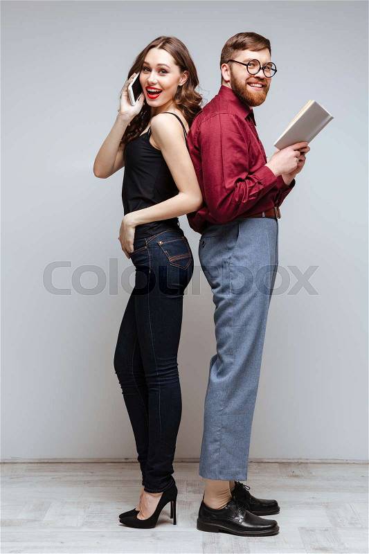 Smiling Woman and Smiling male nerd standing back each other while woman talking on phone and male nerd holding book, stock photo