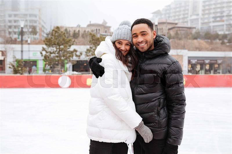 Photo of young cheerful loving couple skating at ice rink outdoors. Looking at camera, stock photo