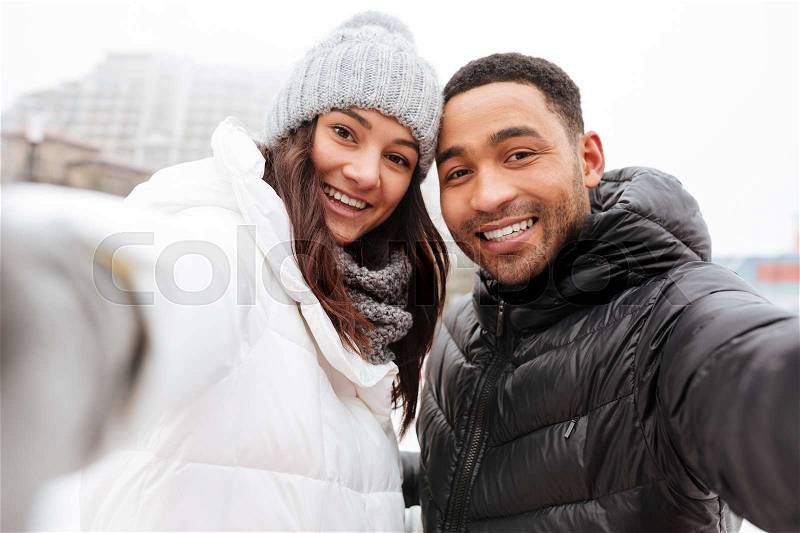 Photo of young happy loving couple skating at ice rink outdoors. Looking at camera and make a selfie, stock photo