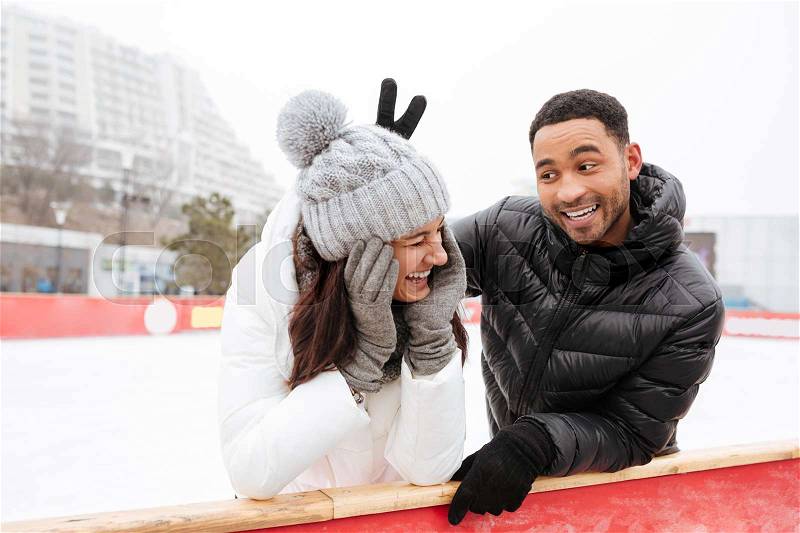 Photo of young happy funny loving couple skating at ice rink outdoors. Looking aside, stock photo