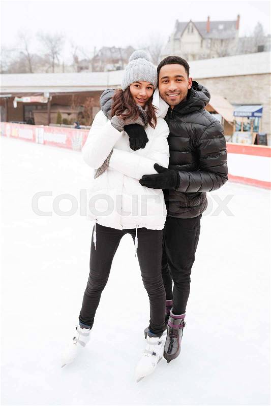 Image of young cheerful loving couple skating at ice rink outdoors. Looking at camera, stock photo