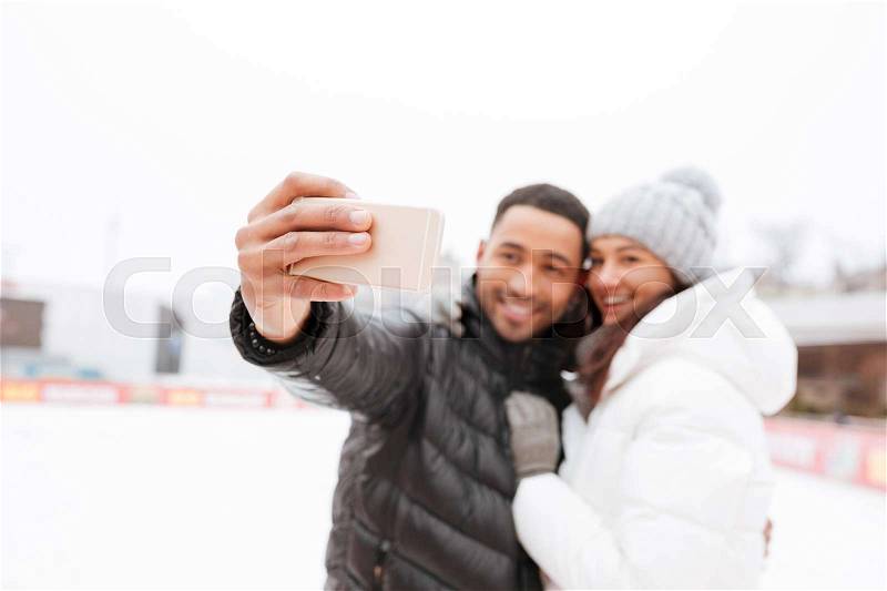 Photo of young cheerful loving couple skating at ice rink outdoors. Make a selfie by phone, stock photo
