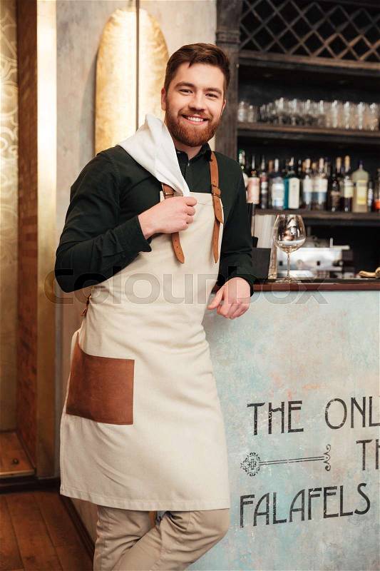 Image of amazing young man bartender standing in cafe. Looking at camera, stock photo