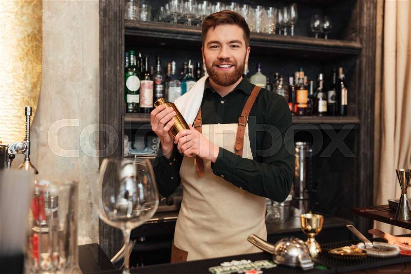 Image of happy young bearded man bartender standing in cafe. Looking at camera holding shaker, stock photo