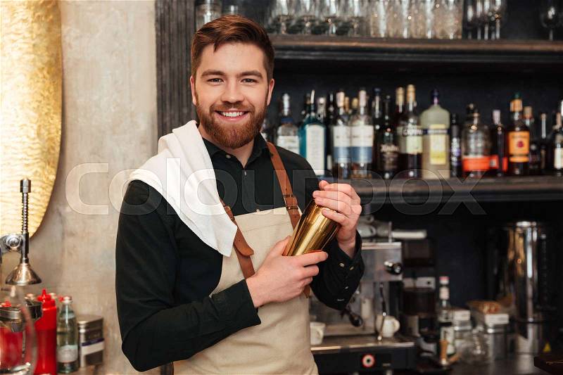 Photo of attractive young bearded man bartender standing in cafe. Looking at camera holding shaker, stock photo