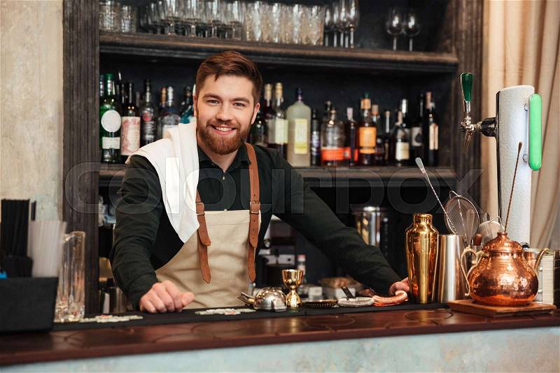 Image of cheerful young bearded man bartender standing in cafe. Looking at camera, stock photo