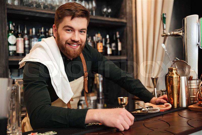 Image of cheerful young bearded man bartender standing in cafe. Looking at camera, stock photo