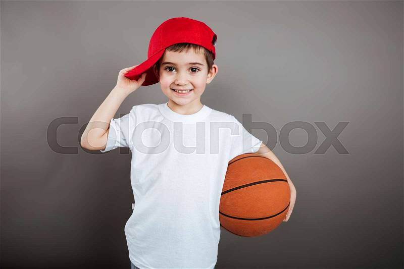 Portrait of cheerful little boy in red cap with basketball ball, stock photo