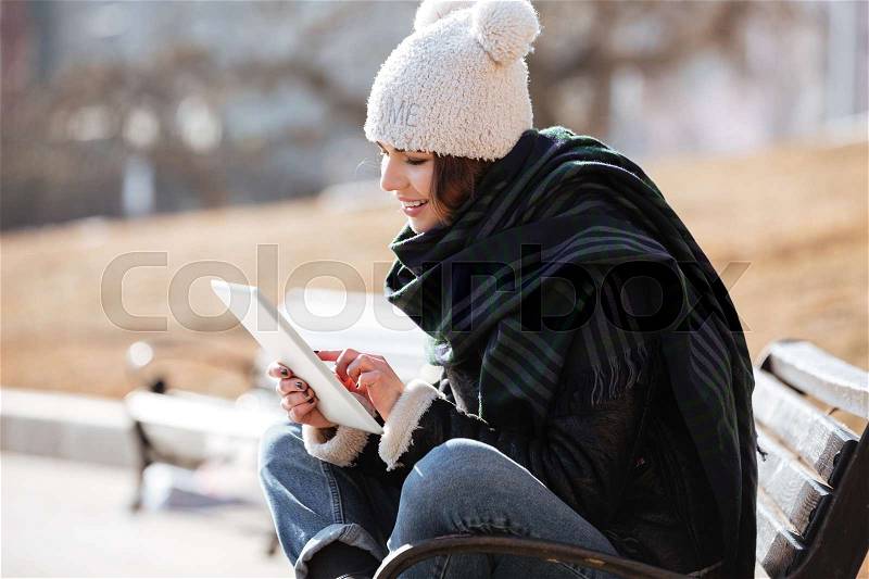Photo of amazing young lady walking on the street wearing hat and scarf while using tablet computer, stock photo