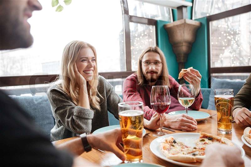Picture of young happy friends sitting in cafe eating pizza while drinking alcohol, stock photo