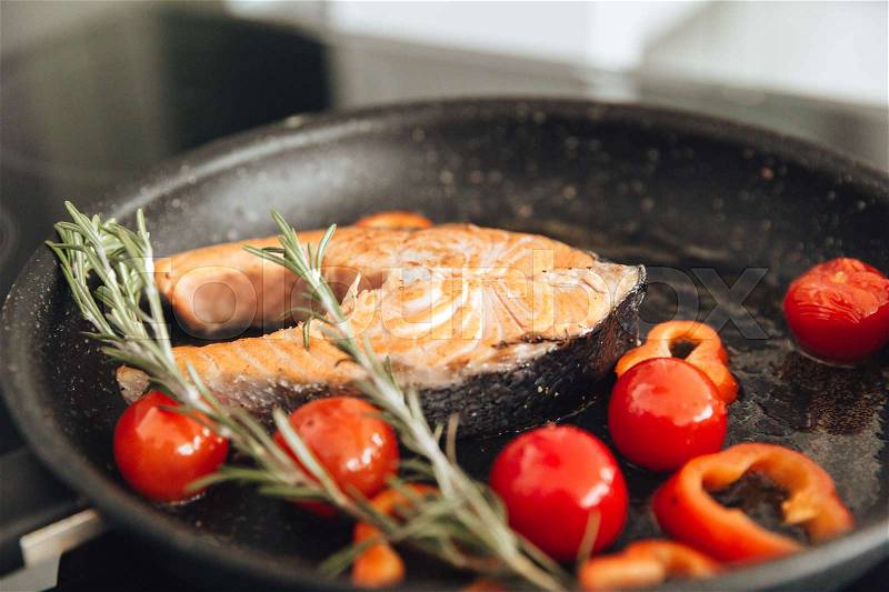 Photo of fish and vegetables on frying pan in kitchen. Cooking concept, stock photo