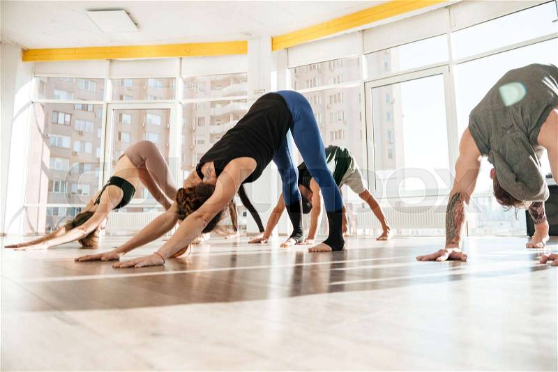 Group of people standing and practicing yoga in studio, stock photo