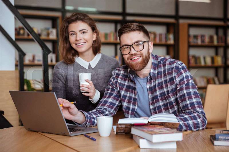 Two happy students with laptop computer networking in library, stock photo