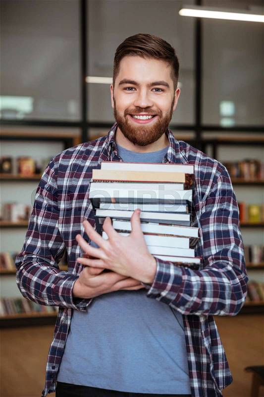 Portrait of a smiling cheerful man student holding books in library, stock photo