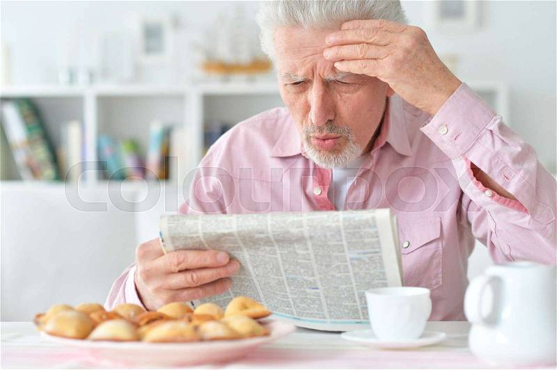 Elderly man reads a newspaper at breakfast, stock photo