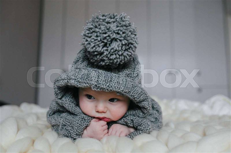 Small baby in knitted clothes lying in the room, stock photo