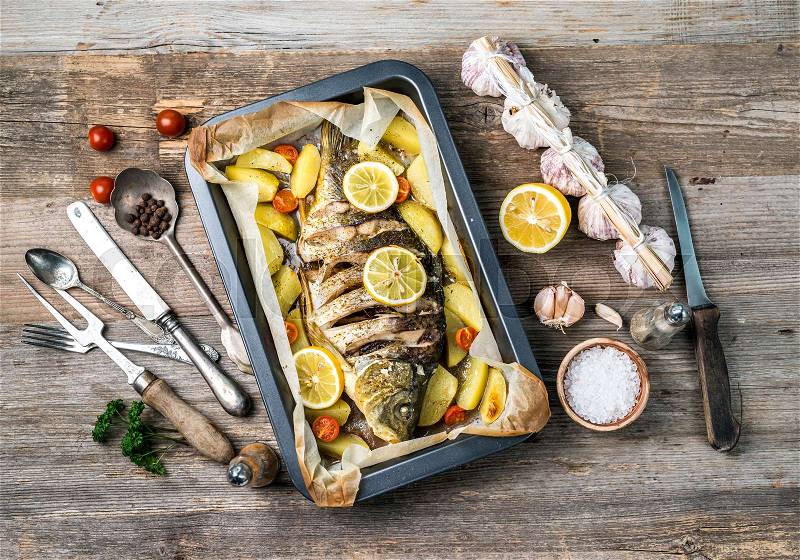 Appetizing baked fish, covered with juicy lemons, garlic and salt on side, topview, stock photo