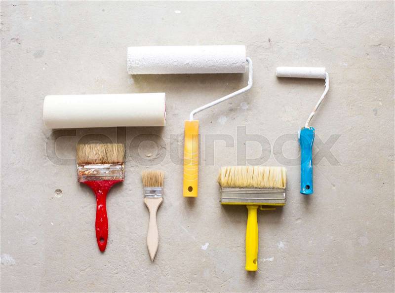 Paint brushes and paint rollers lying on style grey floor, stock photo