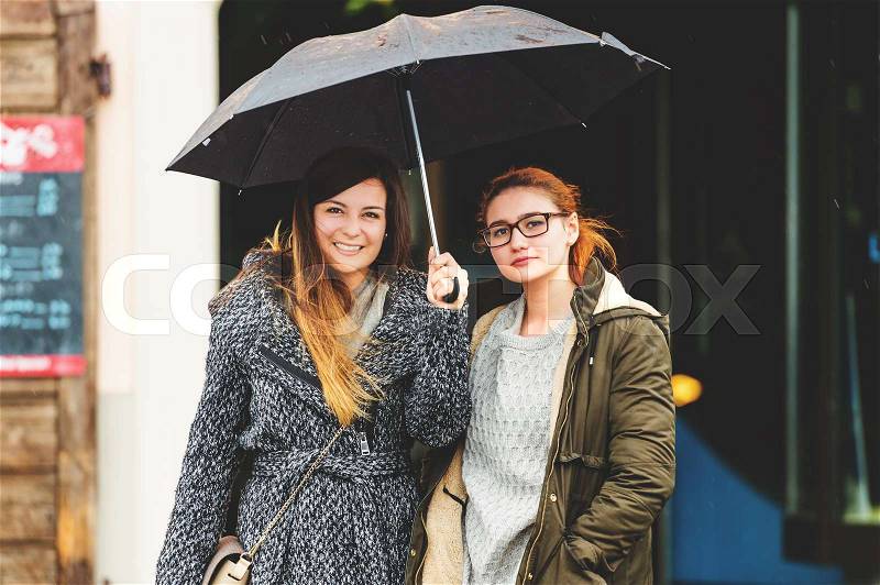 Two 20-25 year old girls under the rain, wearing warm jackets, early spring weather, stock photo