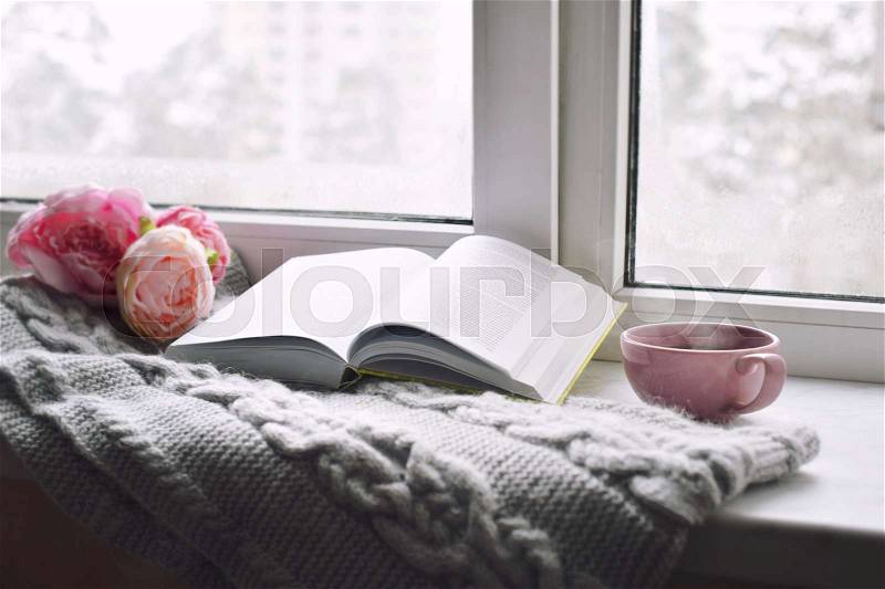 Cozy home still life: cup of hot coffee, spring flowers and opened book with warm plaid on windowsill. Springtime concept, free copy space, stock photo