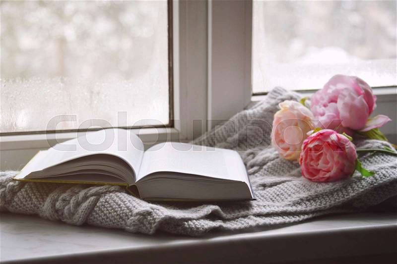 Cozy home still life: spring flowers and opened book with warm plaid on windowsill. Springtime concept, free copy space, stock photo